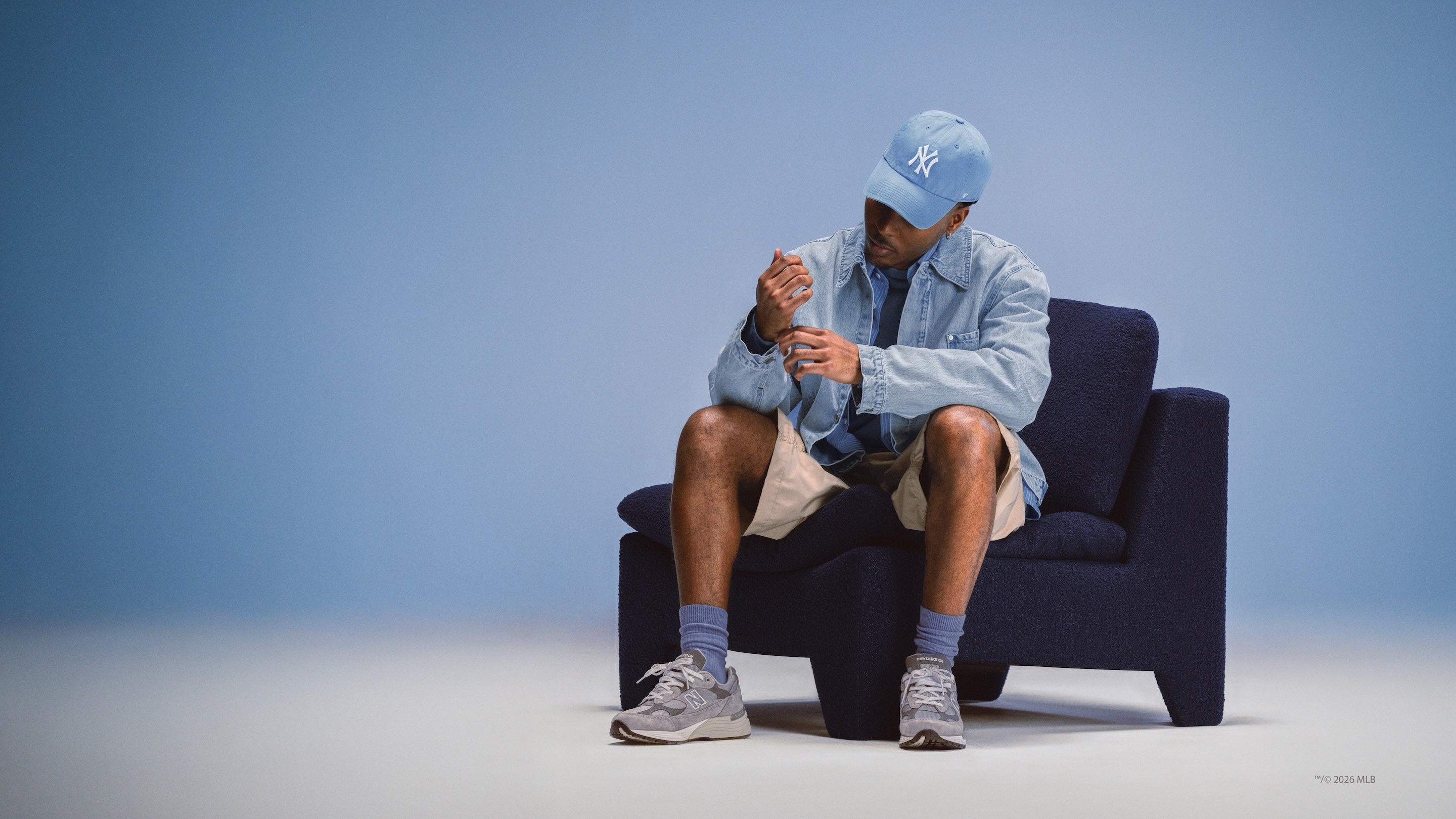 Man wearing a light blue cap and jacket sitting on a dark blue chair against a light blue background