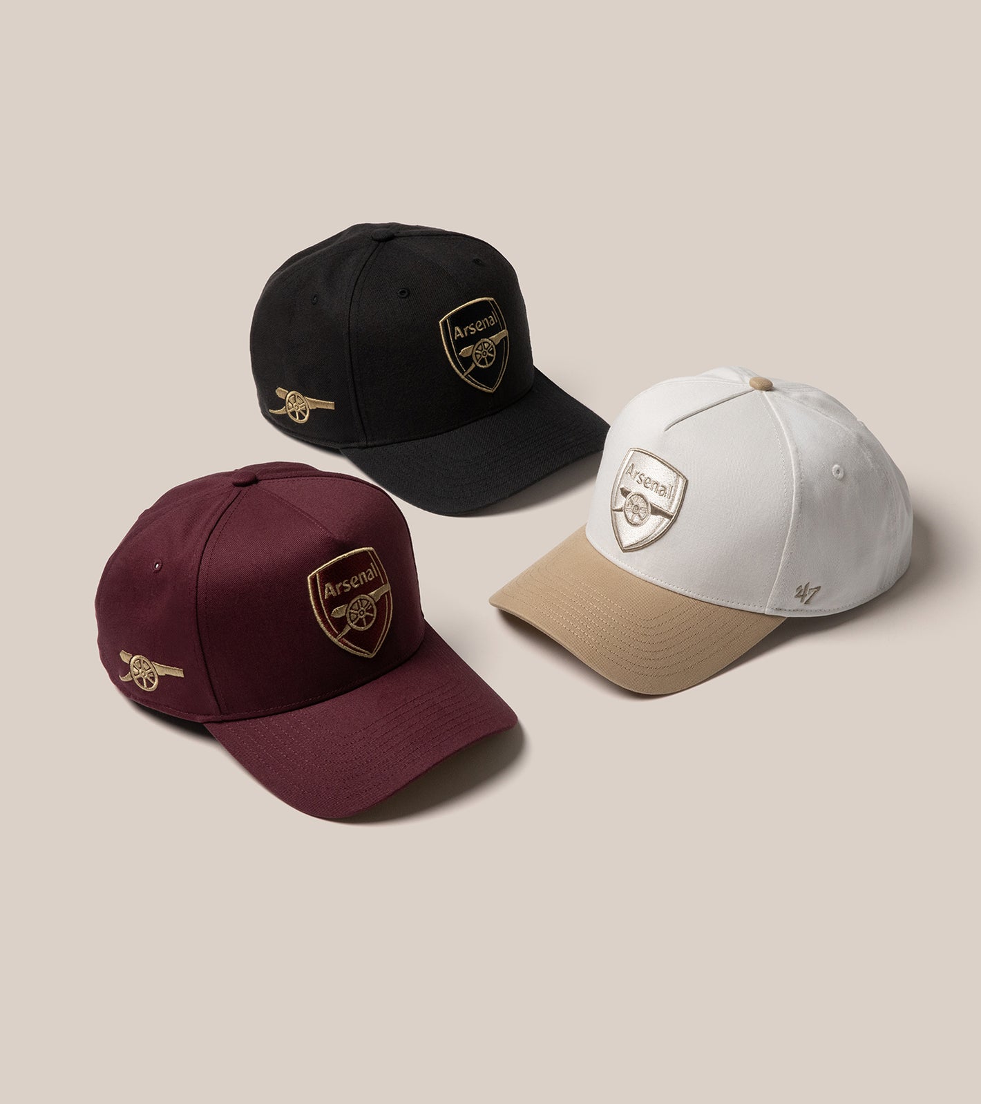 A product image of three Arsenal hats. Maroon and Black with gold Arsenal logos and a white and brown hat with silver logos