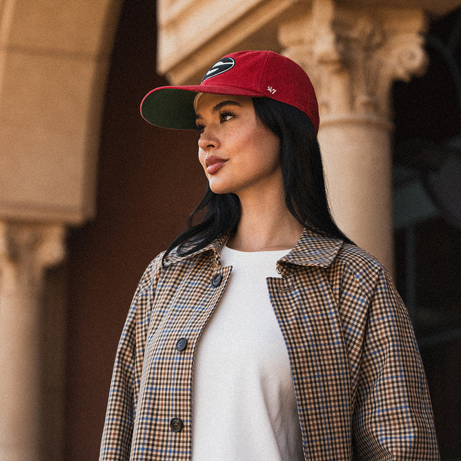 Woman wearing a New York Giants '47 red cap and checkered jacket standing in front of a building.